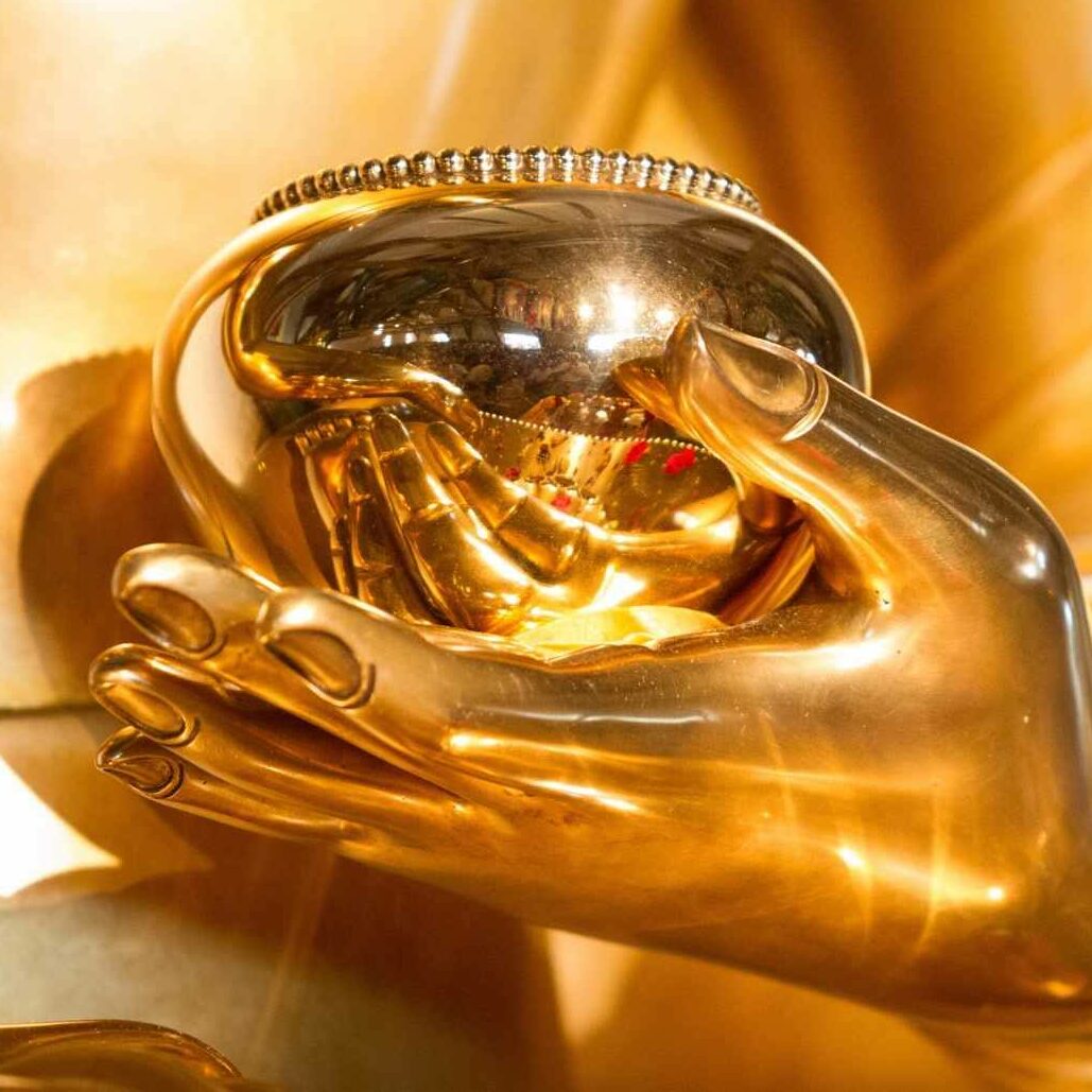 Close-up view of a golden Buddha statue's hand holding a polished alms bowl with intricate details and radiant lighting.